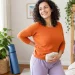 אישה בוגרת מחייכת בעדינות בזמן מתיחה קלה עם כרית חימום ליד הבטן התחתונה